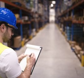 Factory worker holding clipboard and checking inventory of warehouse storage department.